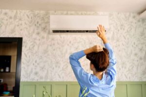 A woman lifting her hair up in front of her air conditioner because it is not blowing cold air