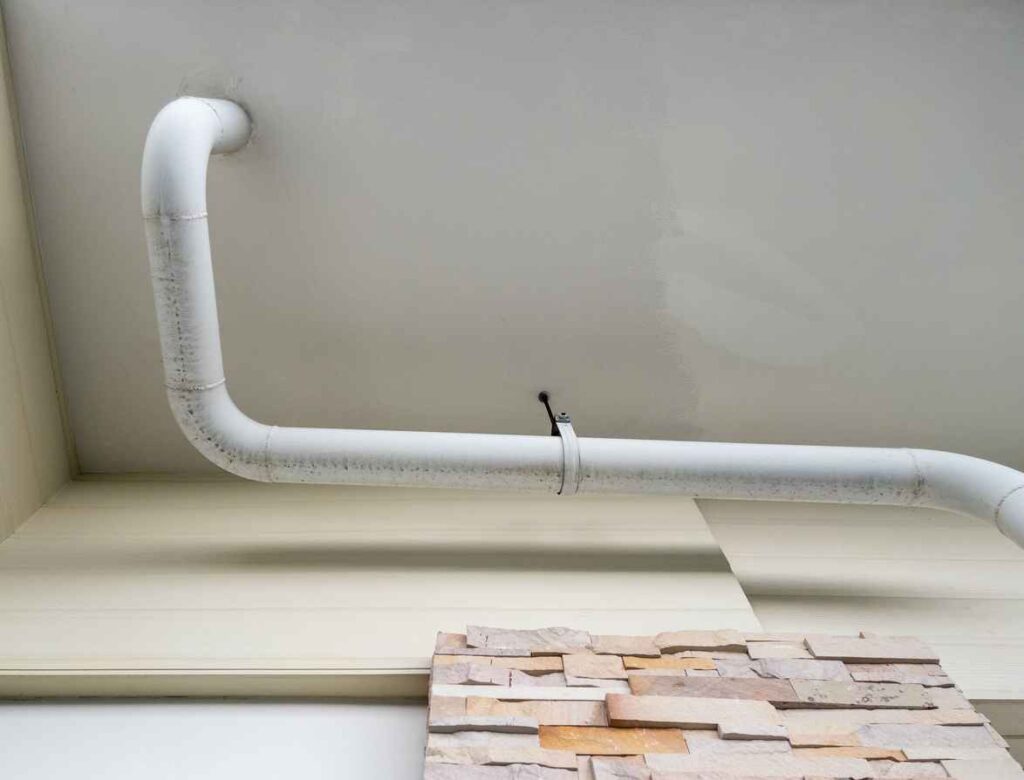 The white curve pipe for drainage of the air conditioner system is hanging on the ceiling of the office building, below the view with the copy space.