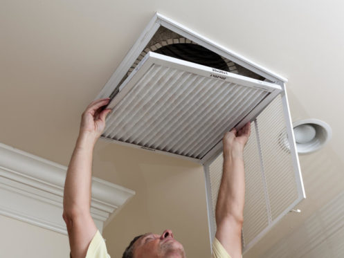 Senior male reaching up to open filter holder for air conditioning filter in ceiling