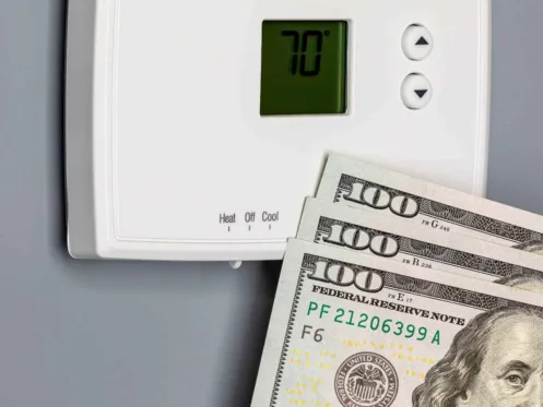 Thermostat with hundred dollar bills in front of it due to a high heating bill.